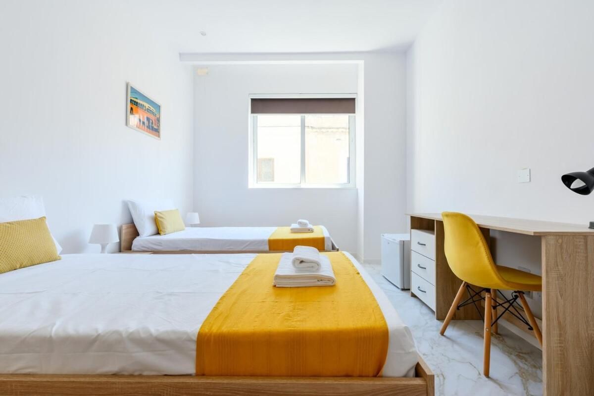 Habitación de hotel con dos camas, un escritorio, una silla, un ventanal y un cuadro en la pared.