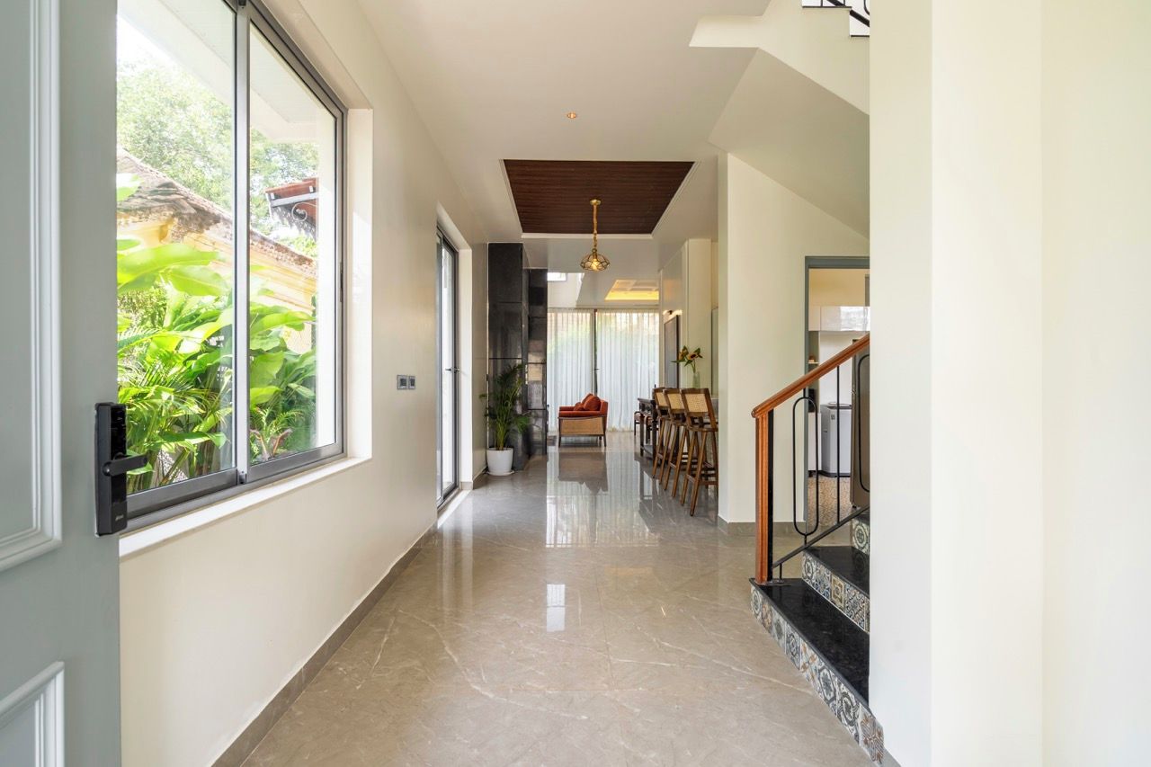 A hallway with a marble floor, a staircase with a wooden handrail, and a view of greenery outside.