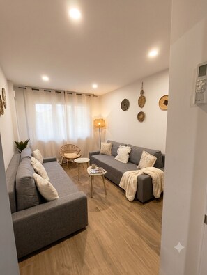 En moderne stue med en grå sofa, en mindre sofa, et rundt bord og en gulvlampe.