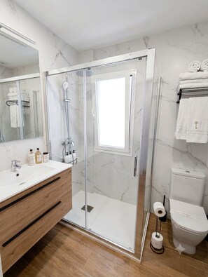Et moderne badeværelse med en glasafskærmet brusekabine, en hvid vask og et toilet.