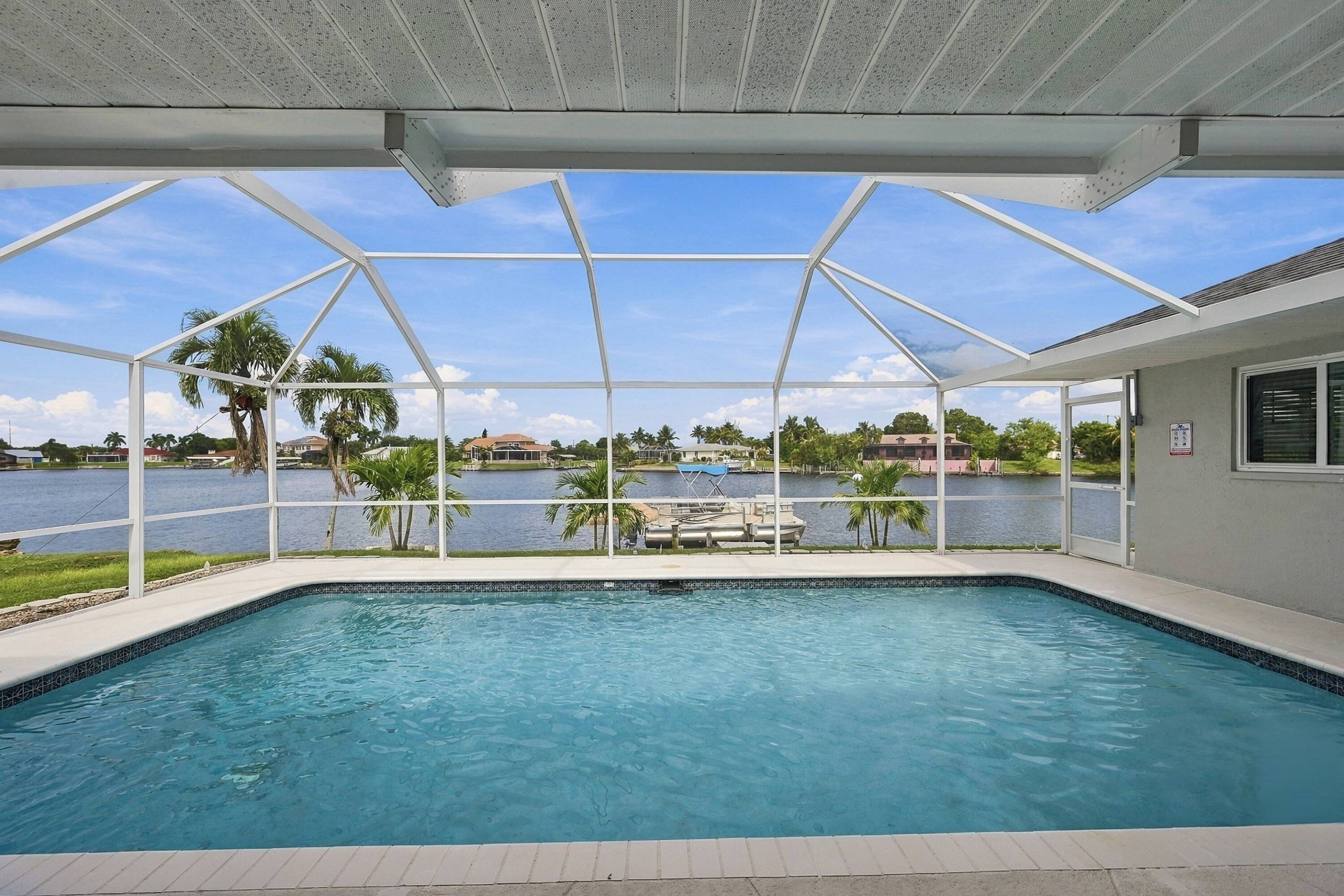 A swimming pool with a view of a lake and boats, surrounded by a covered area with a metal frame and a roof.