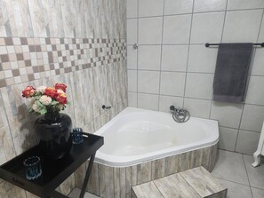 Un baño con una bañera, una mesita con un florero y un perchero para toallas.