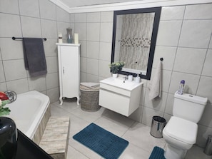 A bathroom with a white sink, mirror, and toilet, a small wicker basket, and a blue rug. - Room-i am a Dedicate, Reliable and Hardw (Matjhabeng)