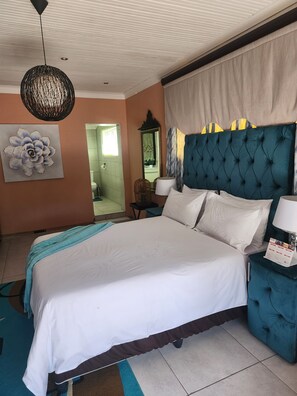 Habitación de hotel con una cama grande, cabecera azul, espejo adosado a la pared y un elemento decorativo en la pared.