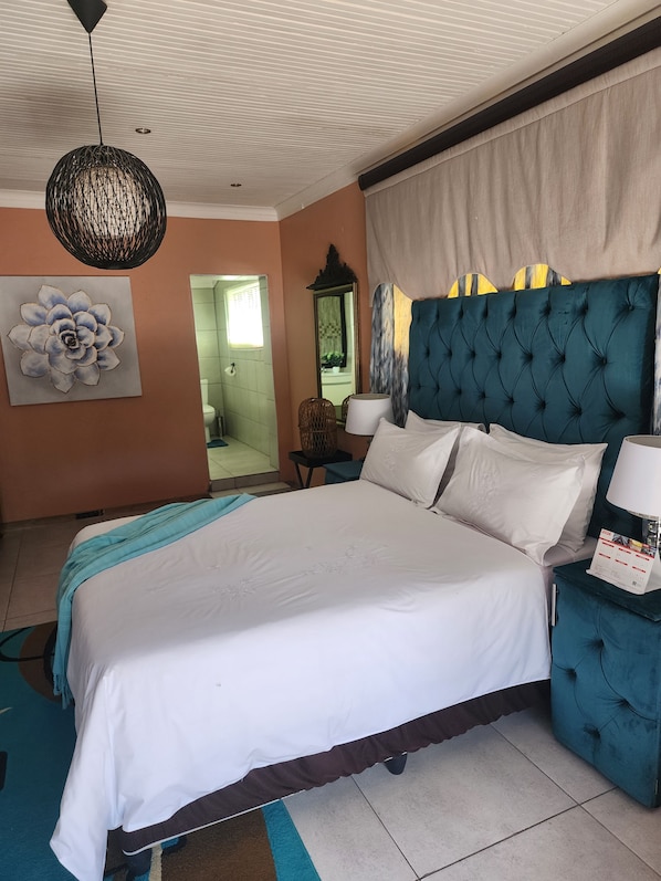 A hotel room with a large bed, a blue headboard, a wall-mounted mirror, and a decorative wall piece. - Room-i am a Dedicate, Reliable and Hardw (Matjhabeng)