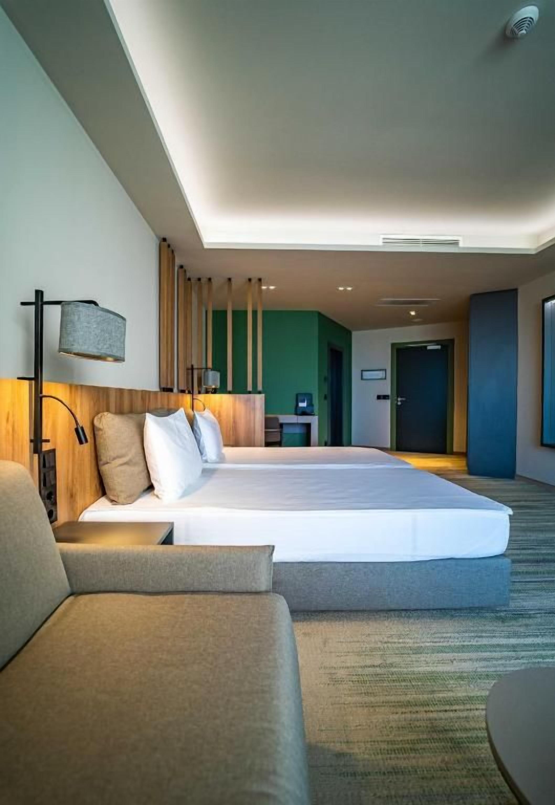 Una habitación de hotel moderna con una cama grande, un sofá, un escritorio y vistas al pasillo.
