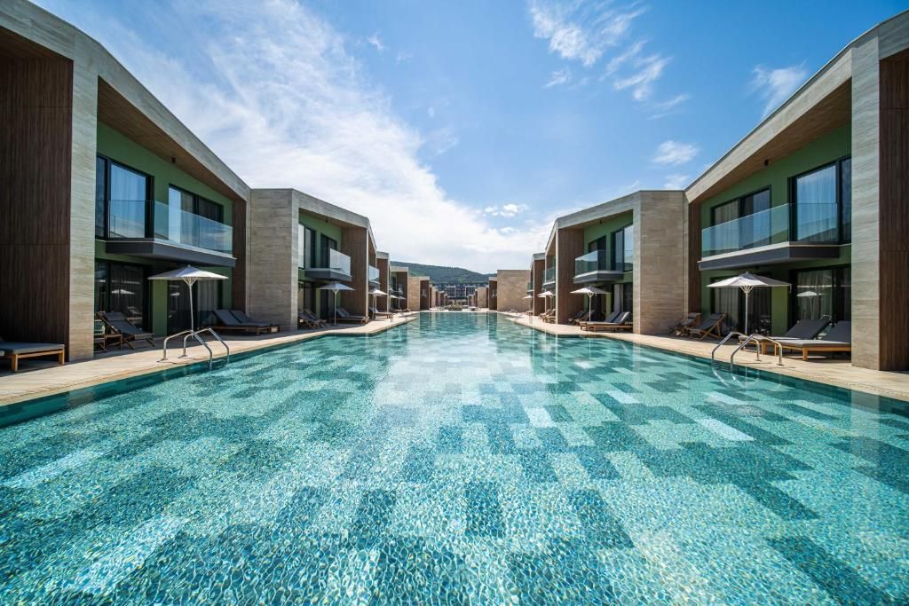 Zona de piscina moderna de un hotel, con una piscina azul cristalina, tumbonas y vistas a colinas distantes.