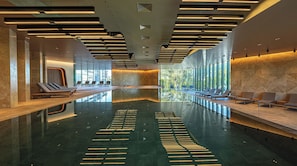 Una piscina interior moderna con sillas de descanso y una barrera de vidrio.
