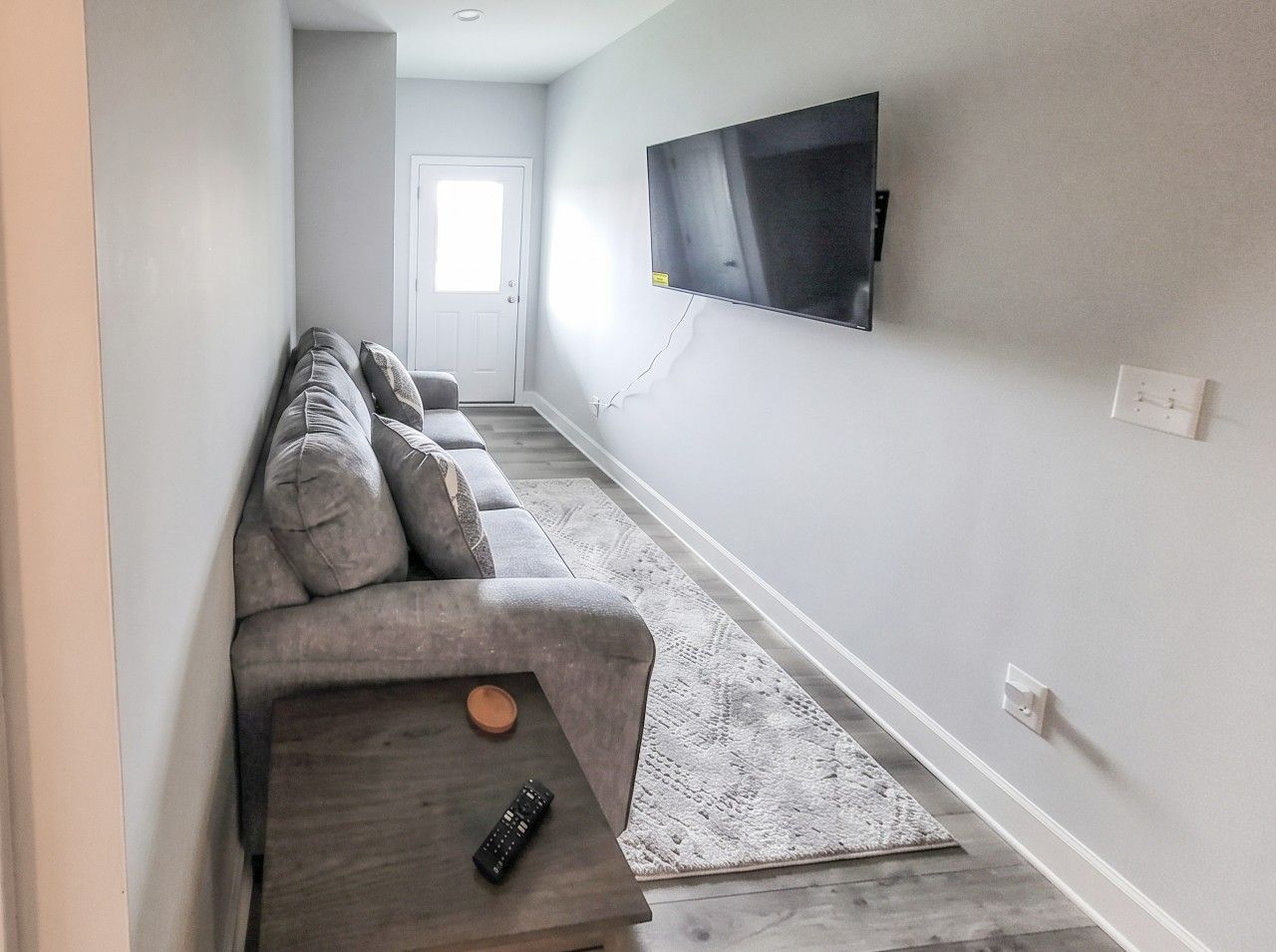 Una sala de estar con un sofá, una mesa de centro, un control remoto y un televisor montado en la pared.