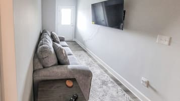 Una sala de estar con un sofá, una mesa de centro, un control remoto y un televisor montado en la pared.