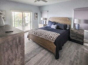Een slaapkamer met een groot bed, een houten hoofdbord, een nachtkastje, een dressoir en uitzicht door een schuifdeur.