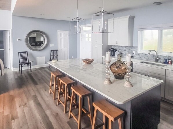 A modern kitchen with a large island, wooden stools, pendant lights, and a view of the outdoors. - 5-Bedroom, 4-Bathroom A-Frame Mountain House (Roaring Gap)