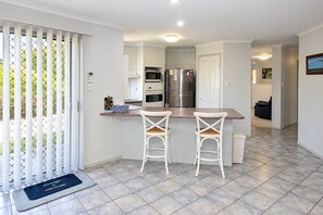 Una cocina moderna con una isla central, dos taburetes de bar, un refrigerador y un horno.
