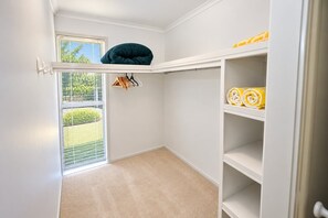Une petite pièce bien éclairée, avec une fenêtre, une étagère au plafond agrémentée d’un coussin et une armoire avec des étagères.