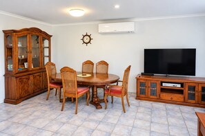 Un comedor con mesa de madera, sillas, un armario y un televisor de pantalla plana.