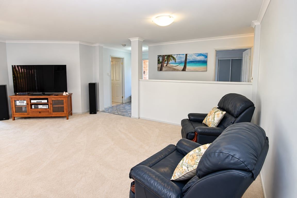Ein Wohnzimmer mit Flachbildfernseher, einer Holzunterhaltungsecke, zwei Ledersofas und einem Gemälde mit Strandmotiv.