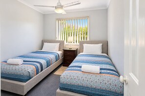 Une chambre avec deux lits, un ventilateur de plafond, une table de chevet et une fenêtre avec des stores.
