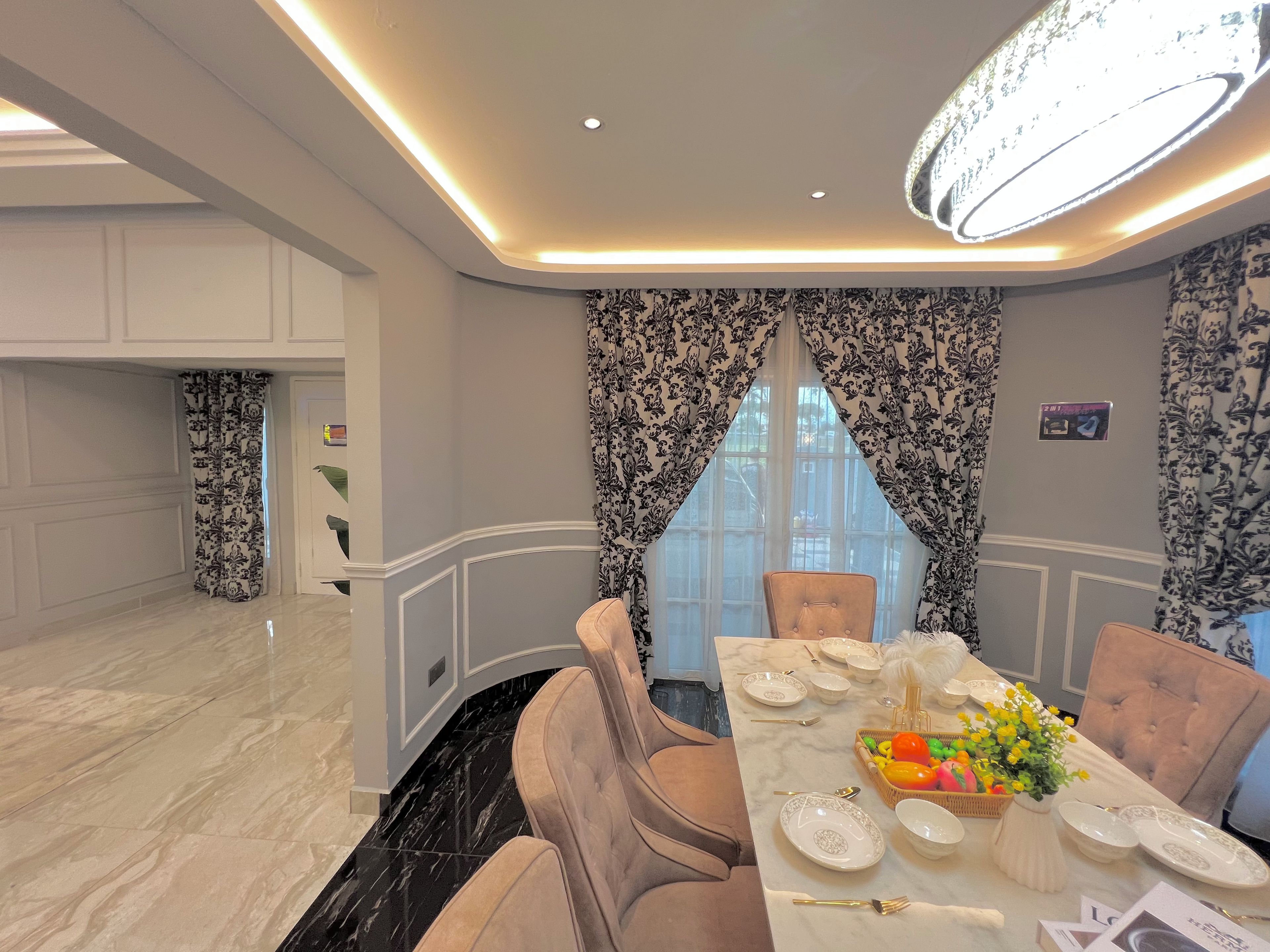 A dining area with a marble floor, a long table set for six, and a chandelier above.