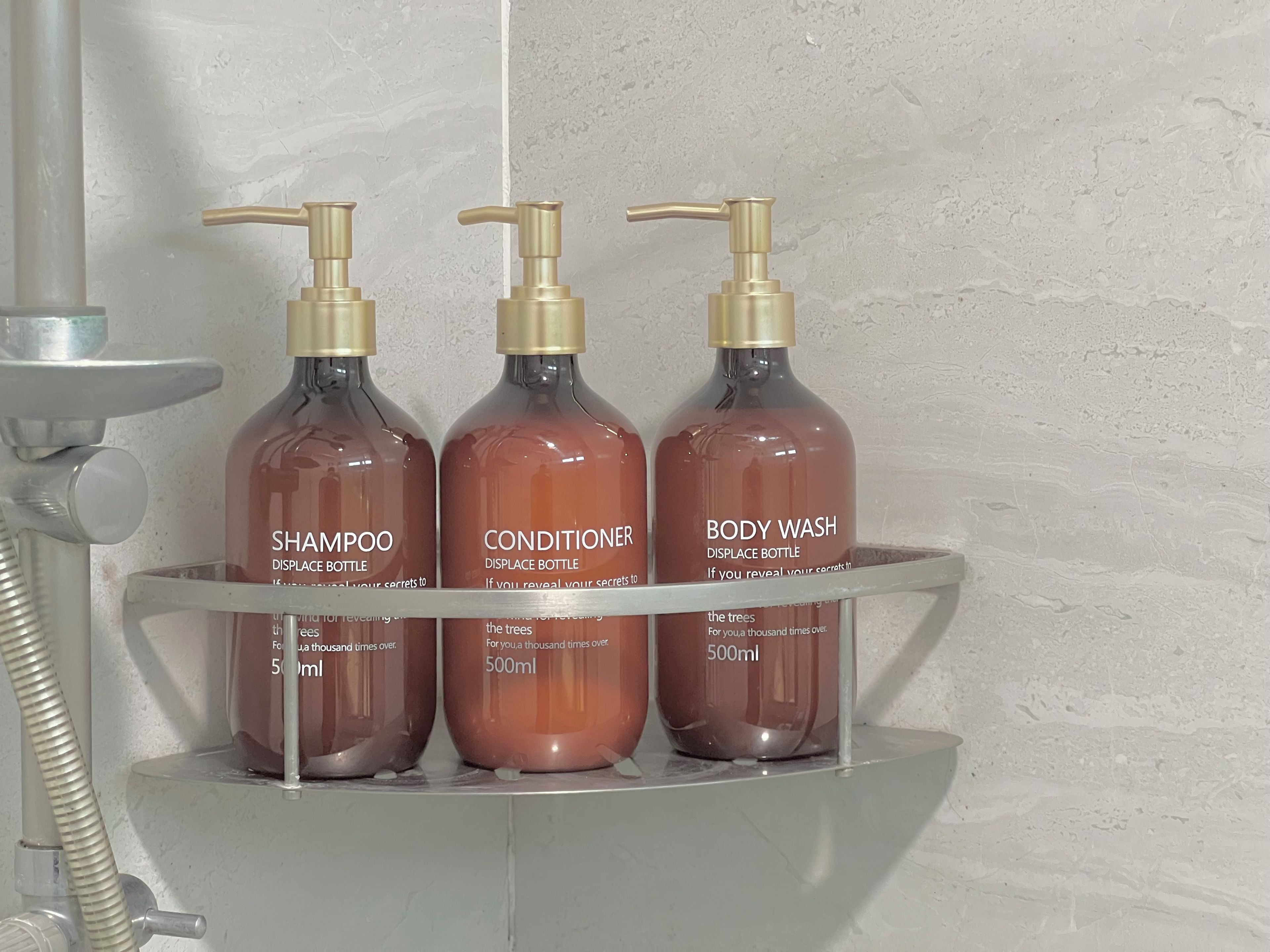 Three bottles of shampoo, conditioner, and body wash on a bathroom shelf.