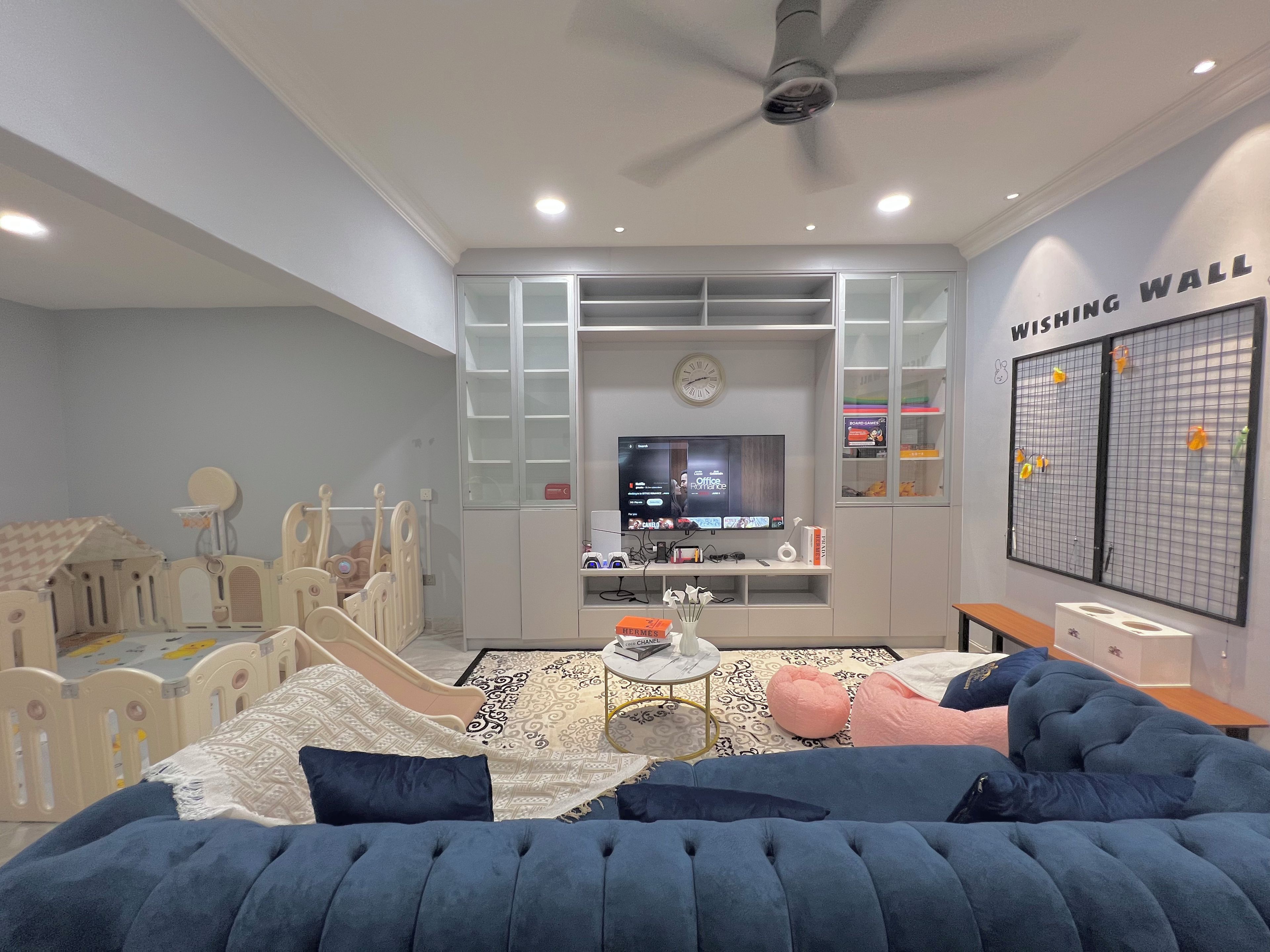 A bedroom with a bed, a television, a ceiling fan, and a wall with a grid pattern.