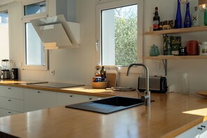 Una cocina moderna con encimera de madera, horno empotrado, pileta y ventana con vista a árboles.