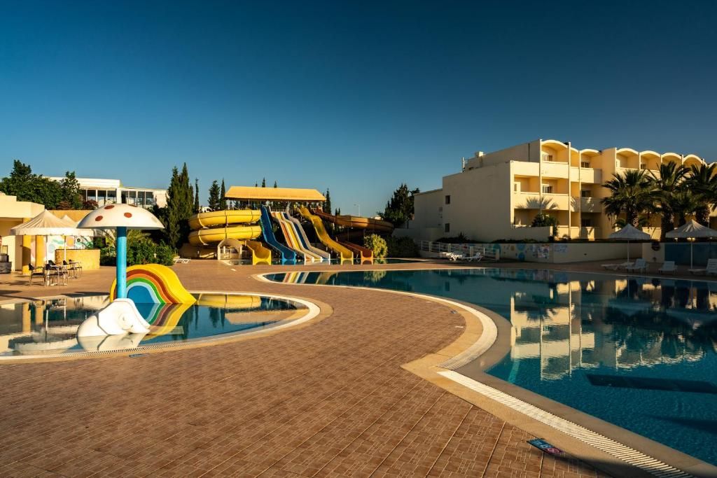 A swimming pool with a slide, a building with balconies, and a clear sky.