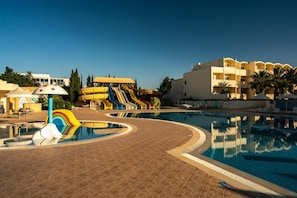 Une piscine avec un toboggan, un bâtiment doté de balcons et un ciel dégagé.