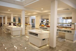 Un comedor moderno de hotel con múltiples estaciones de buffet, techos altos y piso pulido.