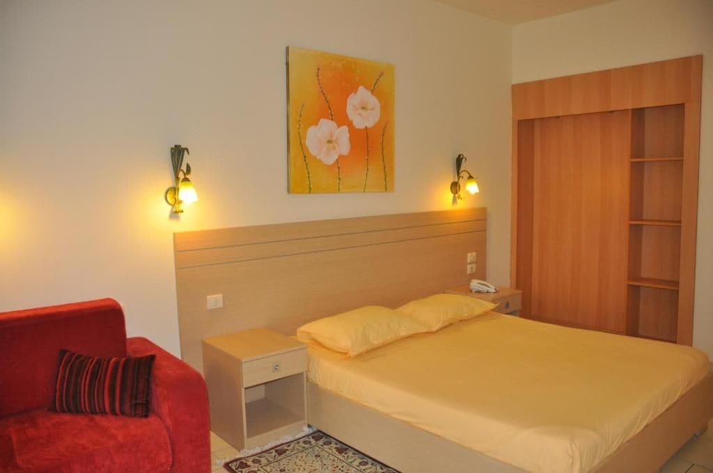 Un dormitorio con cama, mesita de noche, lámpara y una silla roja.