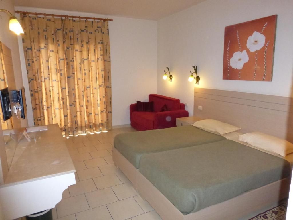 A hotel room with a bed, a red chair, a wall-mounted light fixture, and a painting.
