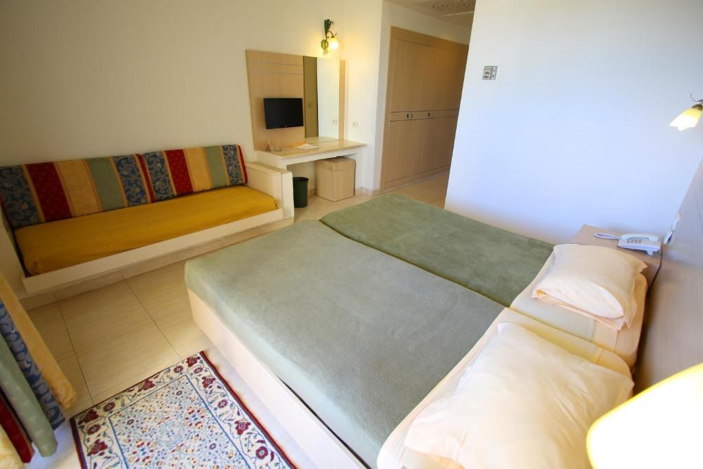 A hotel room with a bed, a sofa, a desk with a TV, and a wardrobe.