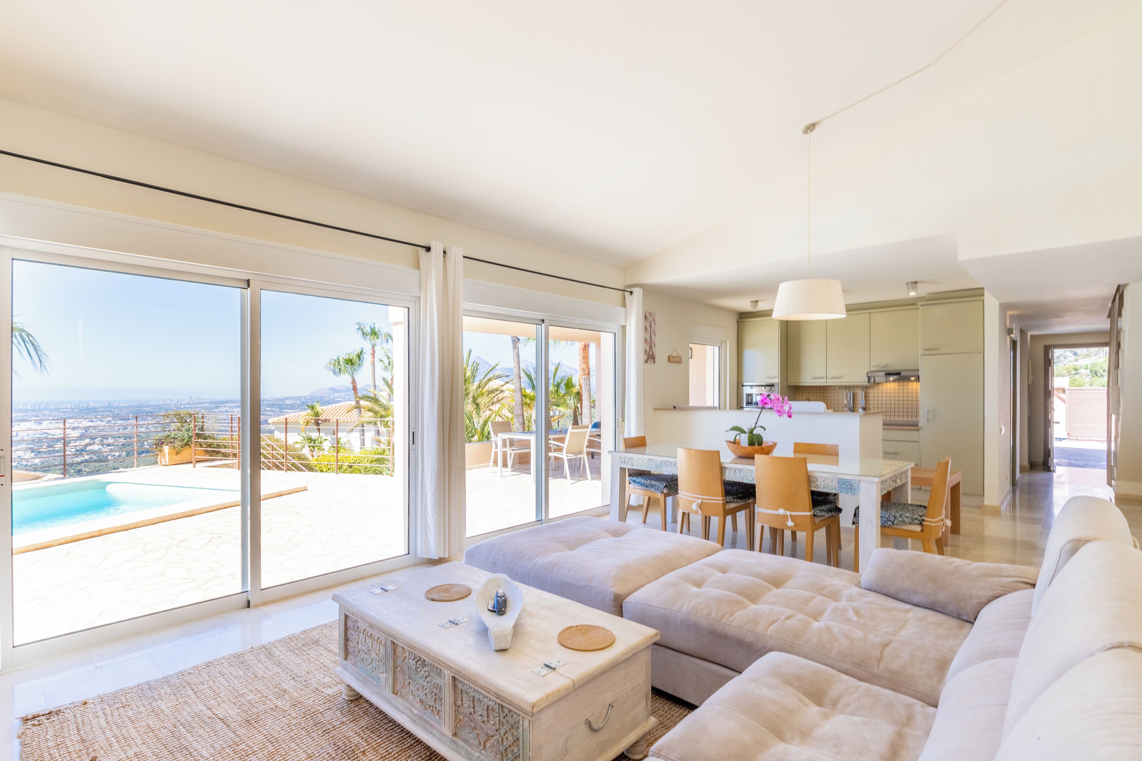 A modern living room with a large sofa, a coffee table, and a view of a swimming pool and mountains.