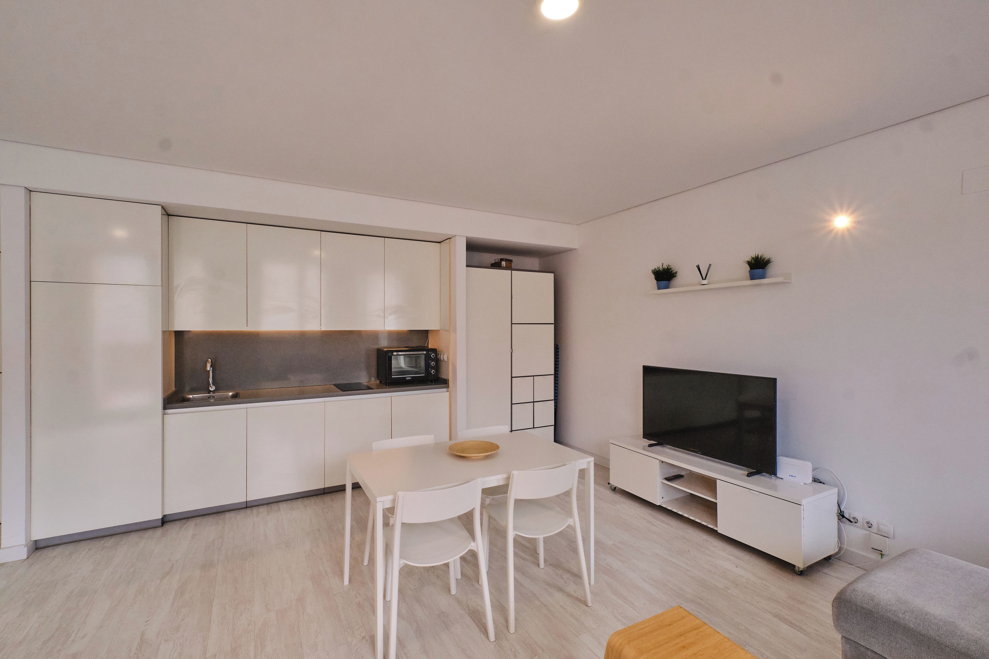 Une cuisine moderne avec des meubles blancs, un four à micro-ondes et un coin repas comprenant une table et des chaises.