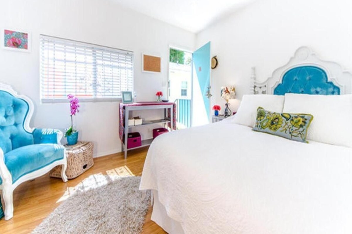Quarto com cama, uma cadeira, uma escrivaninha e uma janela.