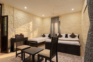 Una habitación con pared de piedra, una cama con almohadas, una mesa con sillas y un ventilador de techo.
