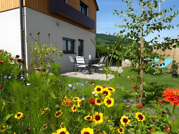 A modern house with a patio, outdoor seating, and a garden with various flowers.