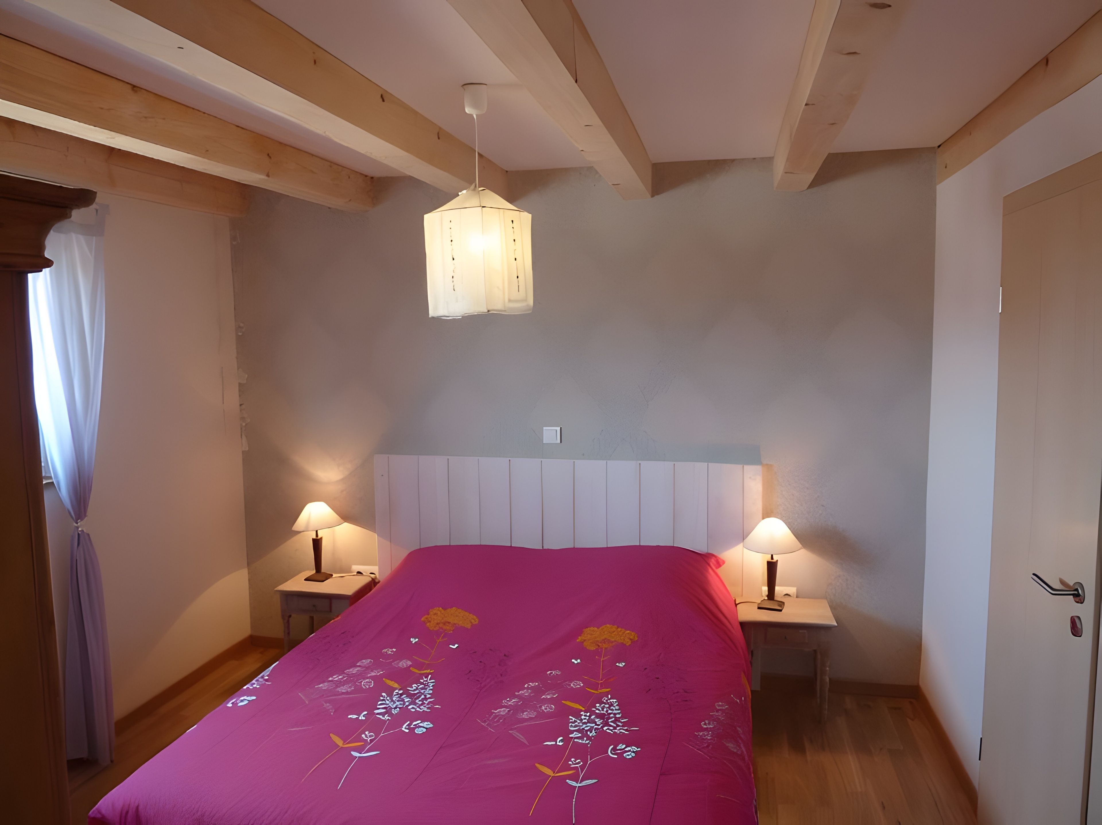 Un dormitorio con techo de madera, una cama con colcha floral rosa, dos lámparas de noche y una lámpara colgante.