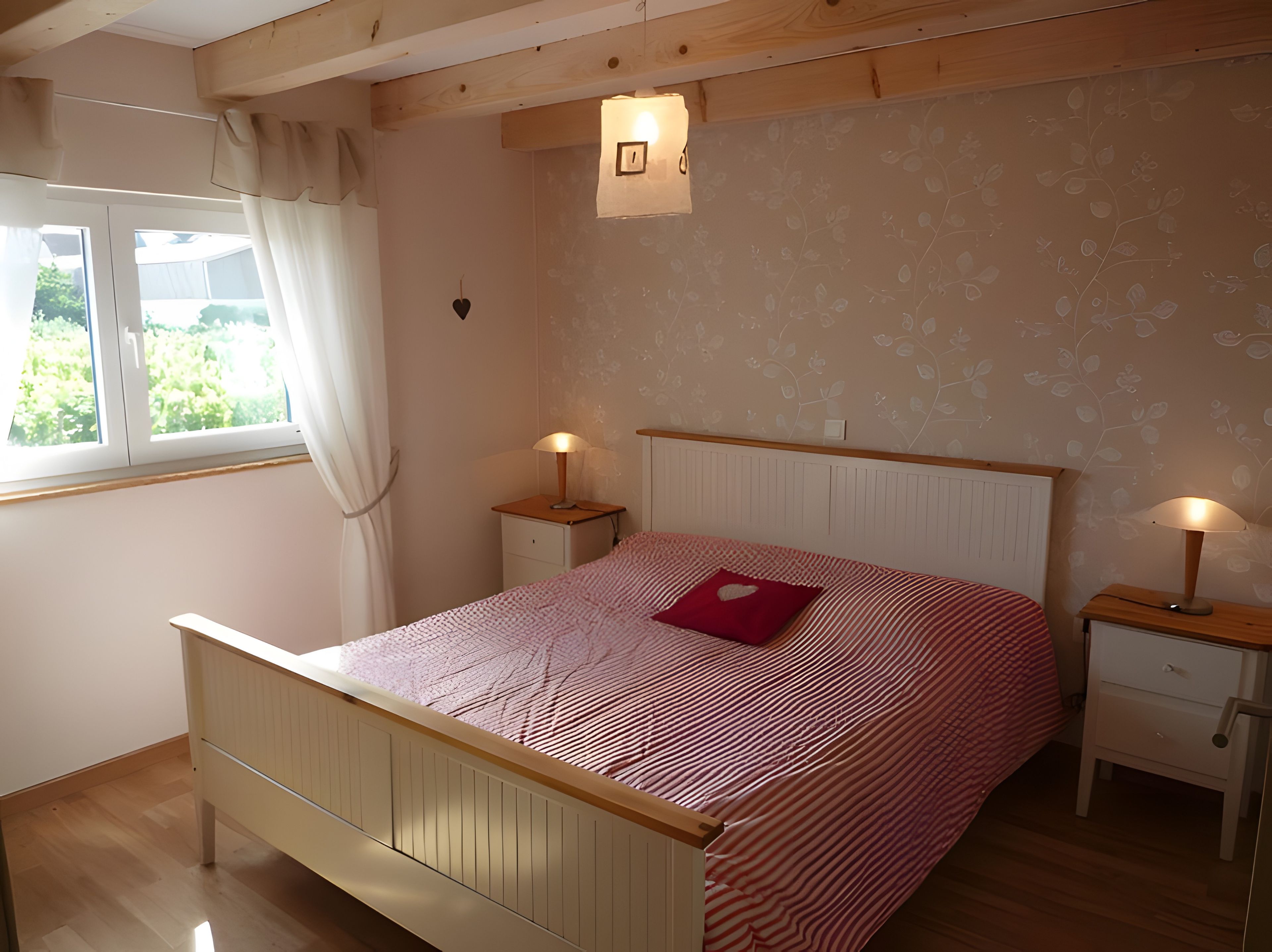 Une chambre à coucher avec un lit en bois, deux tables de chevet avec des lampes, une fenêtre avec des rideaux et un mur orné d’un motif floral.