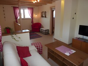 A room with a bed, a red chair, a wooden desk, a television, and a small cabinet.