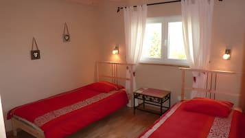 A room with two single beds, a small table, and a window with curtains.