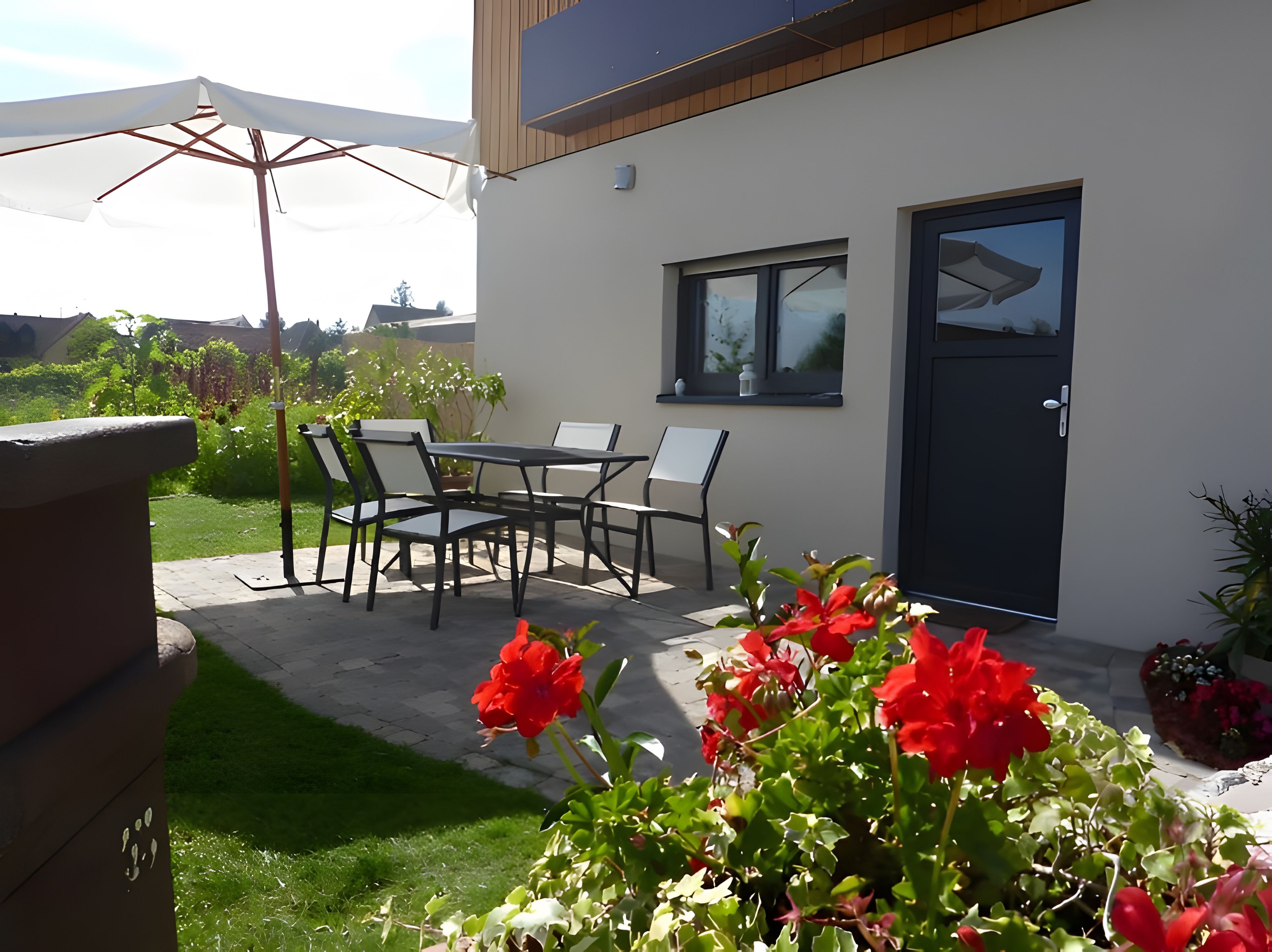 Un patio moderno al aire libre con una mesa, sillas, una puerta y vistas del entorno.