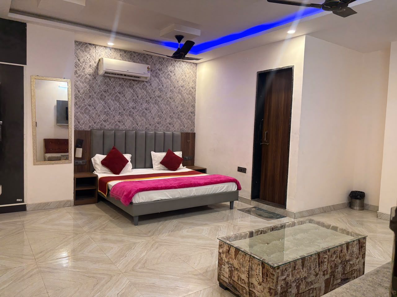 A modern bedroom with a bed, bedside tables, a mirror, and an air conditioning unit.