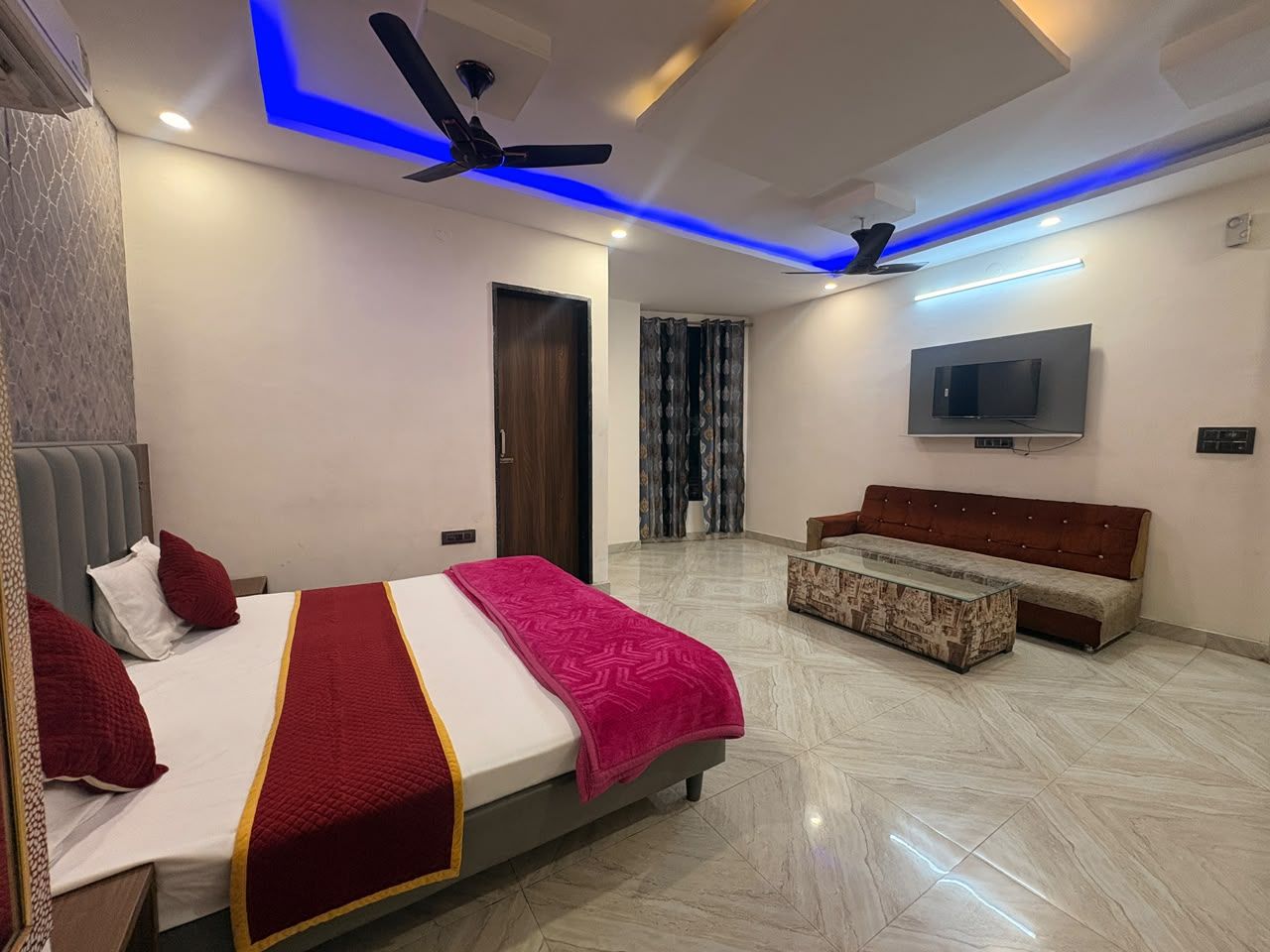Un dormitorio moderno con una cama, un sofá, un televisor y un ventilador de techo.