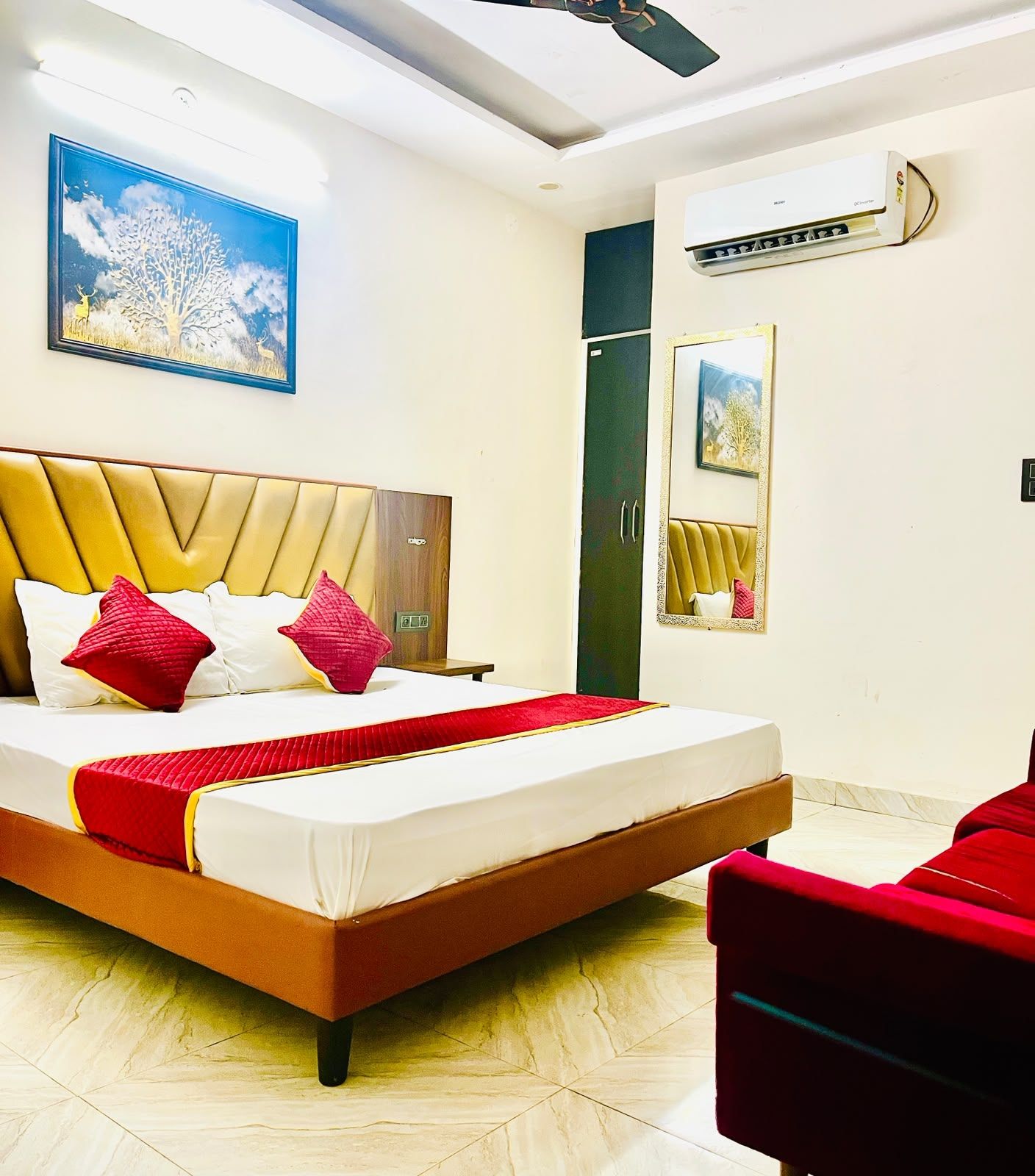 A hotel room with a bed, a red chair, a ceiling fan, and an air conditioning unit.
