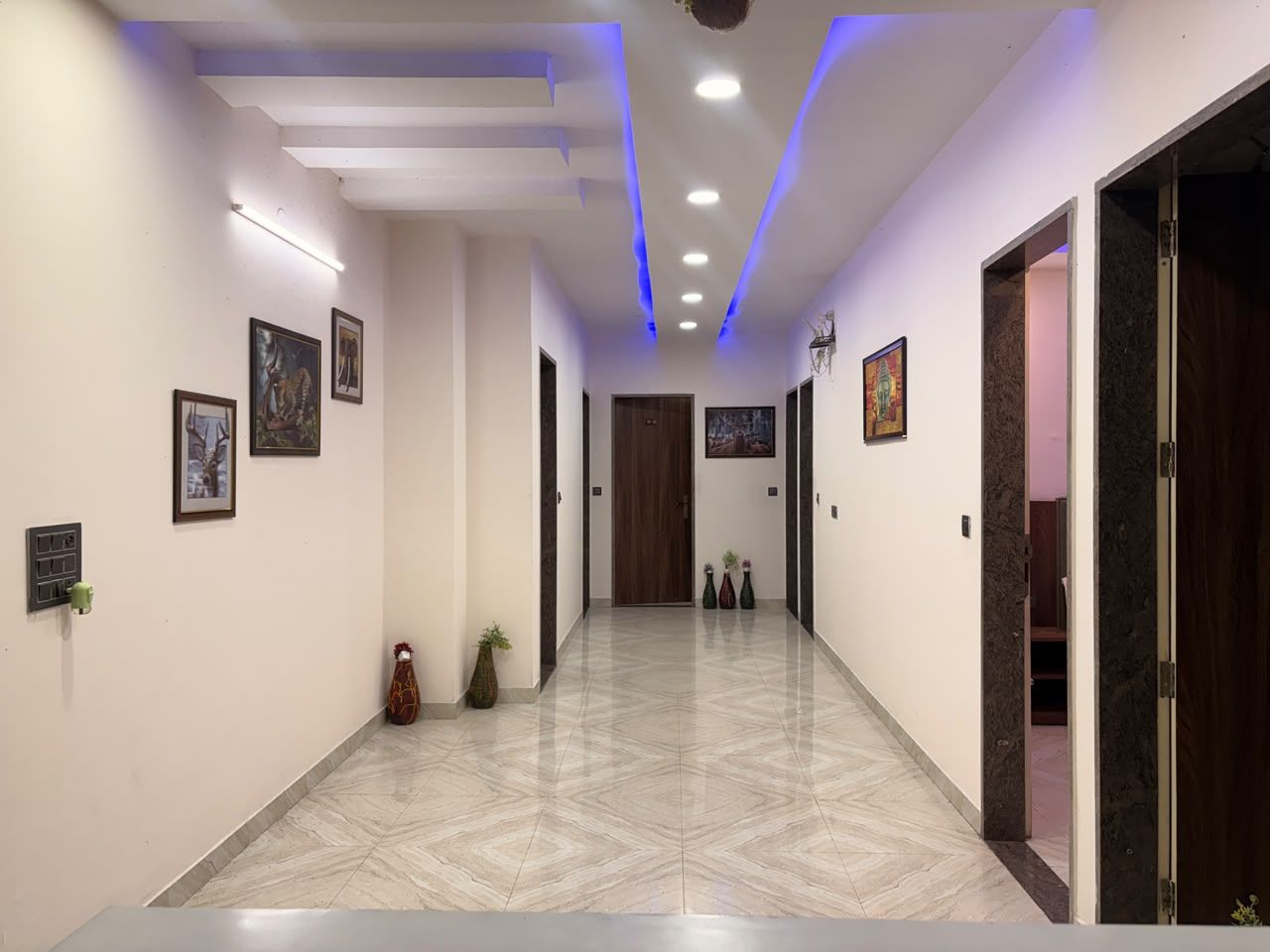 A hallway with a tiled floor, framed artwork on the walls, and a door at the end.