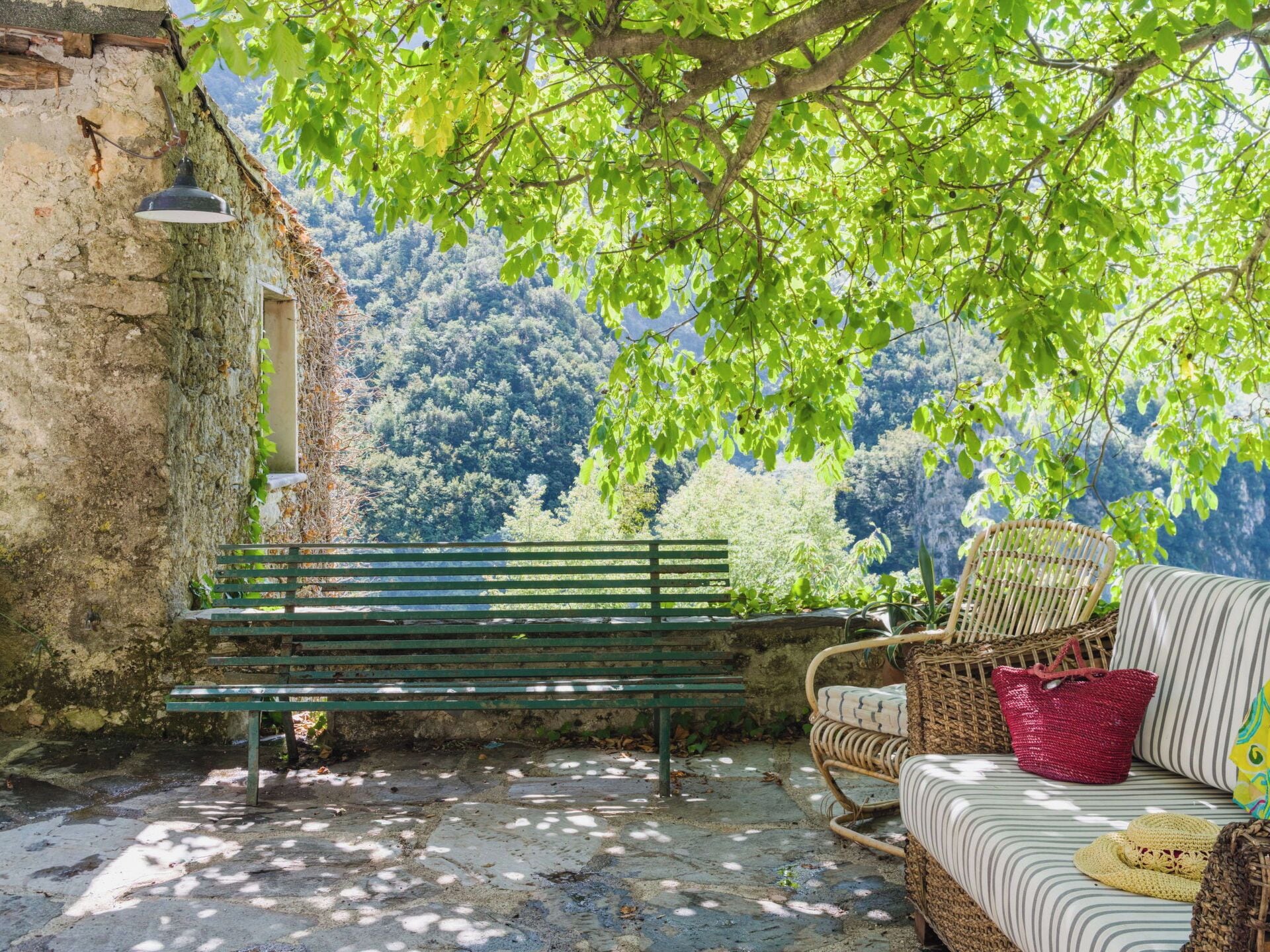 A rustic outdoor seating area with a bench and wicker furniture, overlooking a forested hillside.