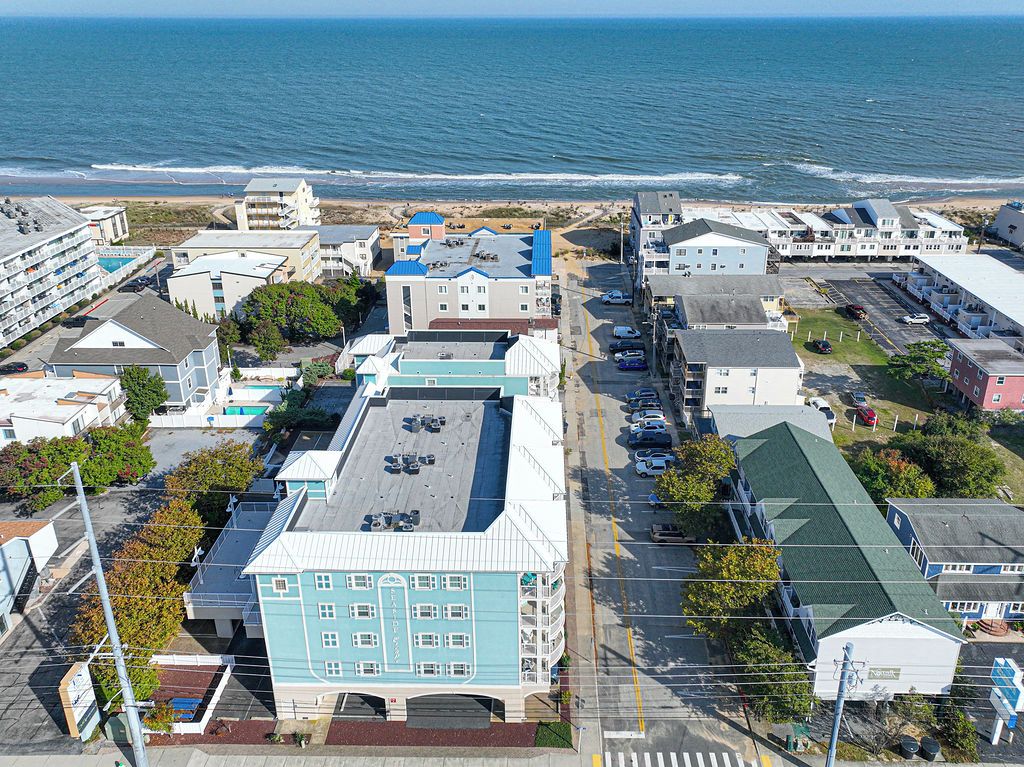 A coastal town with a mix of residential and commercial buildings, a parking lot, and a view of the ocean.