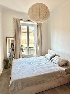 Ein Schlafzimmer mit einem großen Bett, einem Nachttisch, einer Hängeleuchte und einem Fenster mit Vorhängen.