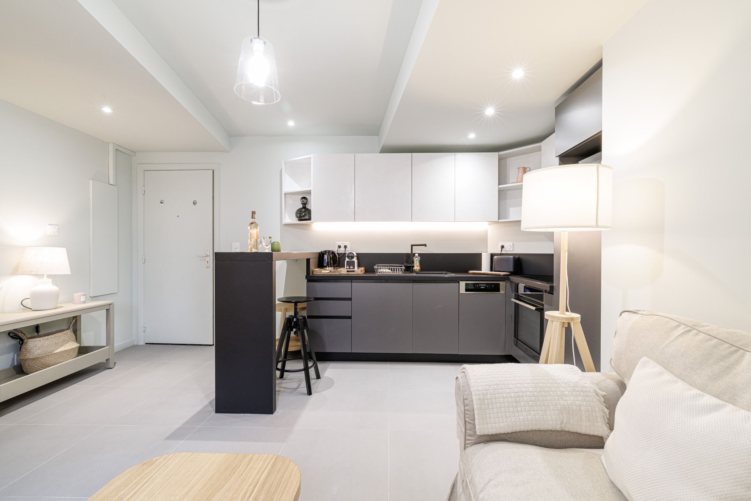 Een moderne keuken met een centraal eiland, een eethoek met tafel en stoelen, en een woonkamer met een bank en een lamp.