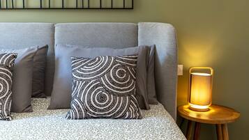 Un lit avec une literie à motifs, une œuvre d’art représentant des feuilles accrochée au mur et une table de chevet avec une lampe.